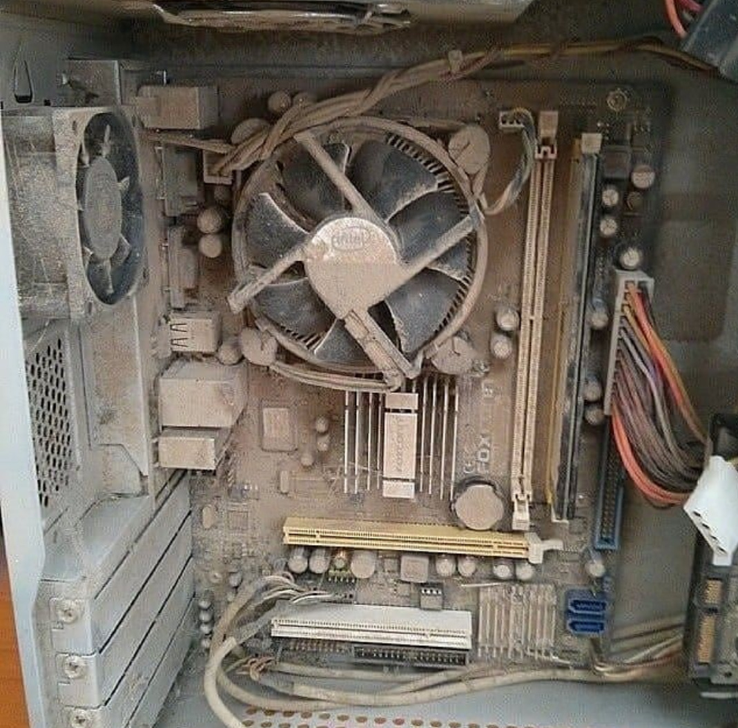 Wnętrze bardzo zakurzonego komputera stacjonarnego z widoczną płytą główną, radiatorem procesora, wentylatorem i przewodami.
