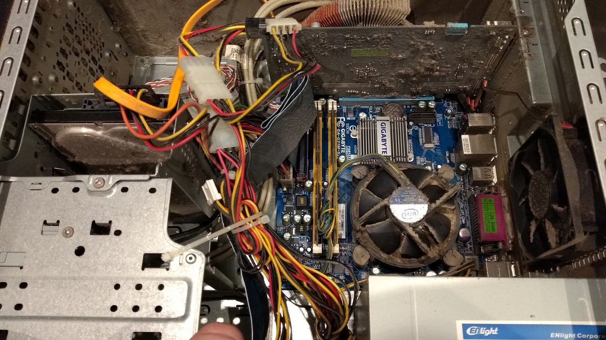 Wnętrze zakurzonego komputera stacjonarnego z widoczną płytą główną Gigabyte, kartą graficzną, dyskiem twardym i plątaniną kolorowych kabli.