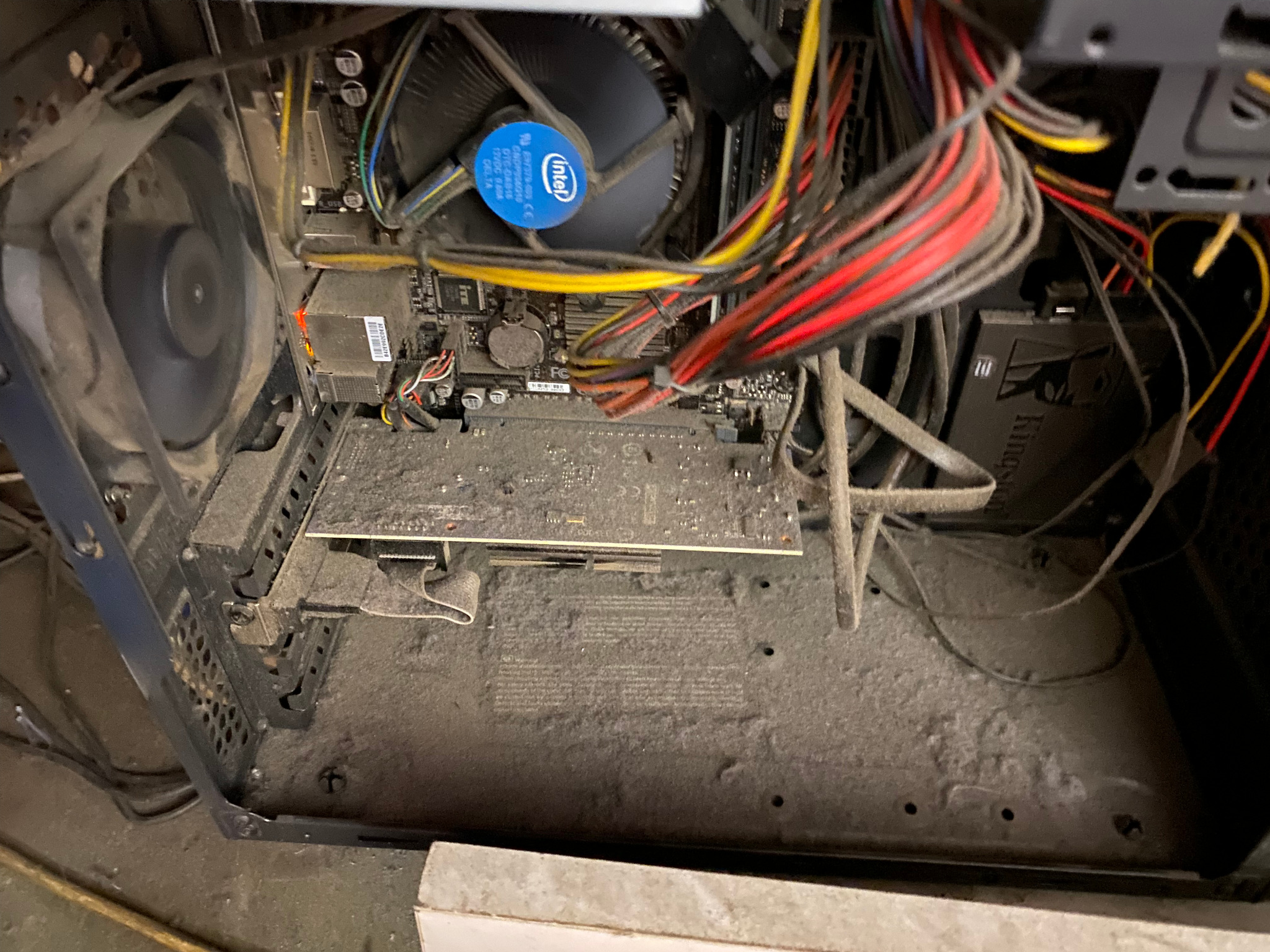 Wnętrze bardzo zakurzonego komputera stacjonarnego z widocznym radiatorem procesora Intel, kartą graficzną i kablami zasilającymi. Kurz pokrywa wszystkie elementy, włącznie z wentylatorami i płytą...