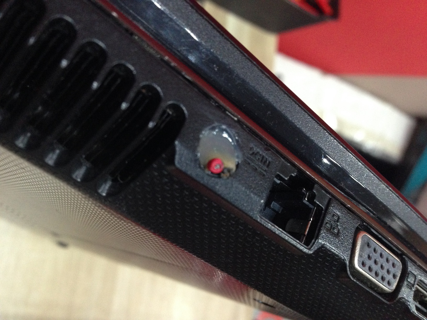 Uszkodzone gniazdo zasilania DC-IN w laptopie, zalane substancją klejącą, widoczne porty LAN i VGA.