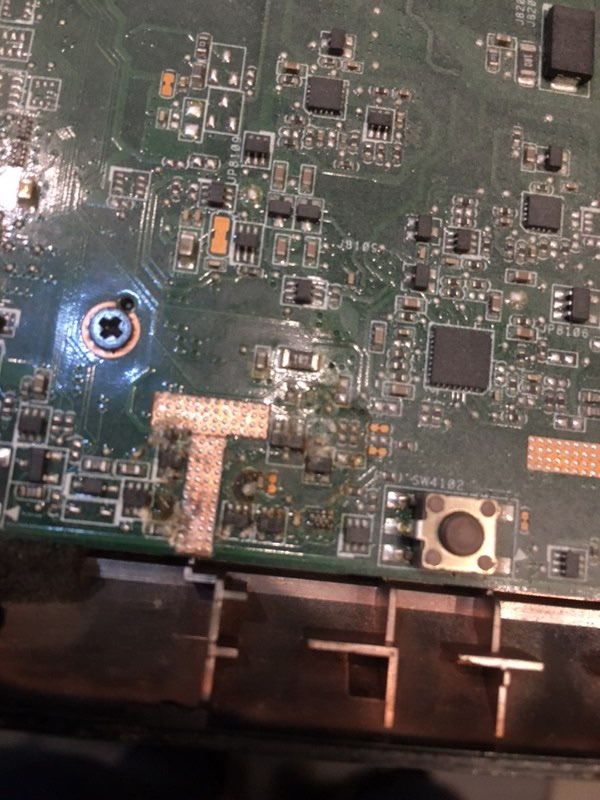 Zbliżenie uszkodzonej płyty głównej laptopa z widocznymi śladami korozji i przepalonymi elementami.