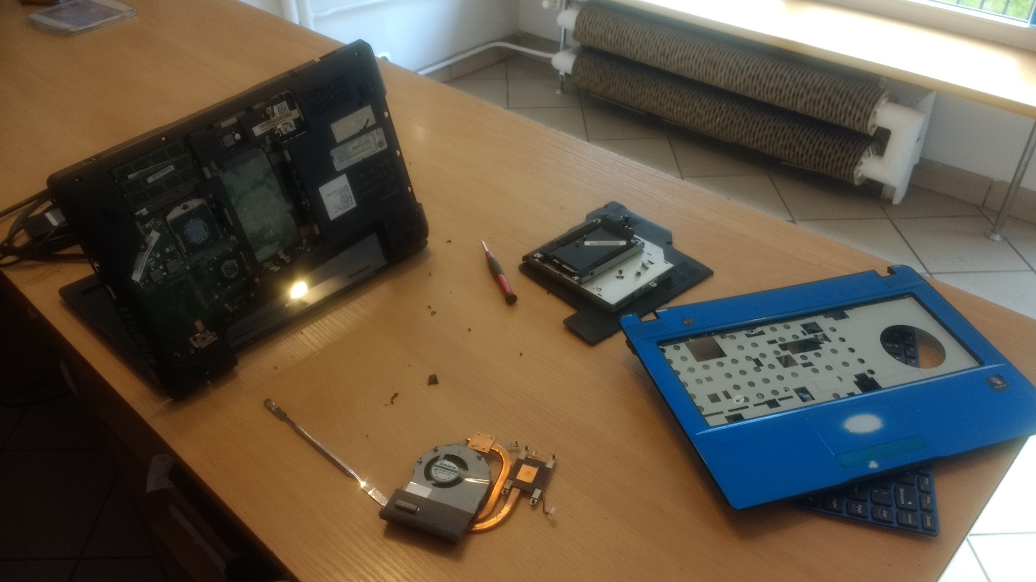 Rozłożony laptop na biurku w Łodzi, widoczne elementy wewnętrzne: płyta główna, chłodzenie, obudowa. Mały śrubokręt leży obok dysku twardego.