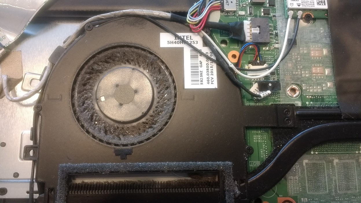 Wnętrze laptopa z widocznym, zakurzonym wentylatorem chłodzącym procesor, płytą główną i kablami.