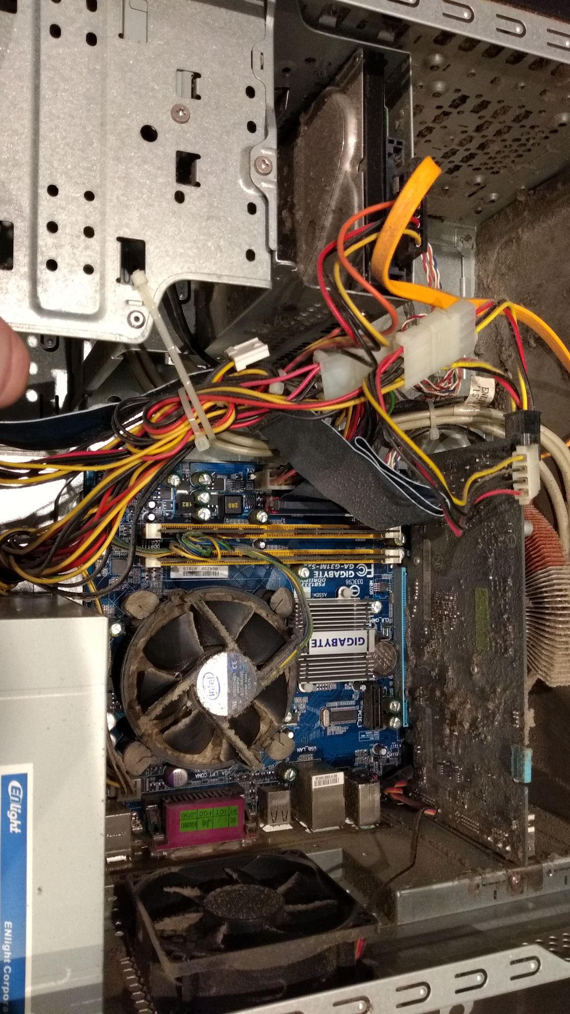 Wnętrze brudnego komputera stacjonarnego z zakurzoną płytą główną Gigabyte, widoczne liczne kable, wentylator procesora Intel pokryty kurzem, karta graficzna i inne komponenty. Zaniedbany stan...