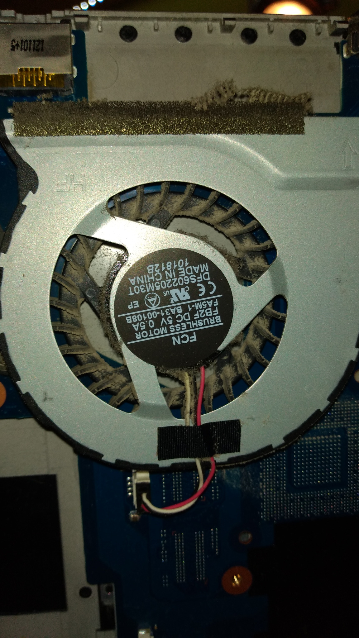 Wnętrze laptopa z widocznym, zakurzonym wentylatorem chłodzącym procesor, model FCN FB2F DC 5V 0.5A, z widocznymi kablami zasilającymi i fragmentem płyty głównej.