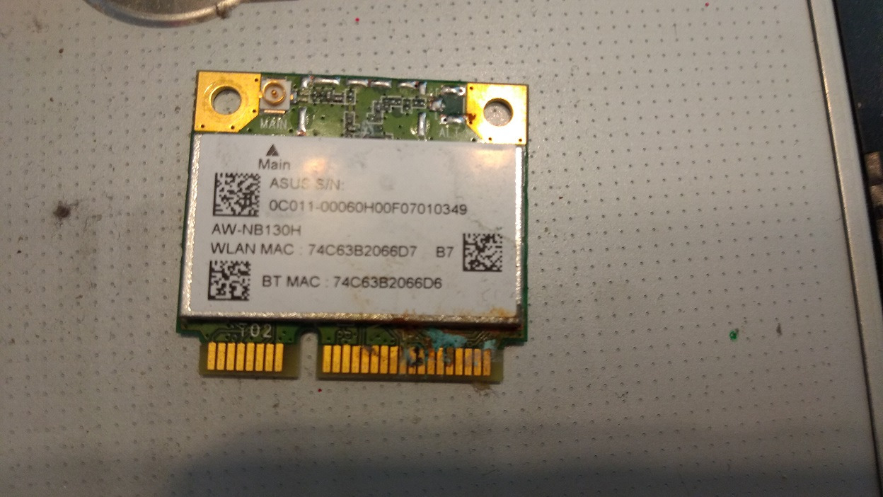 Uszkodzona karta sieciowa ASUS AW-NB130H z widocznymi śladami korozji na złączu, leżąca na metalowej powierzchni z perforacją.