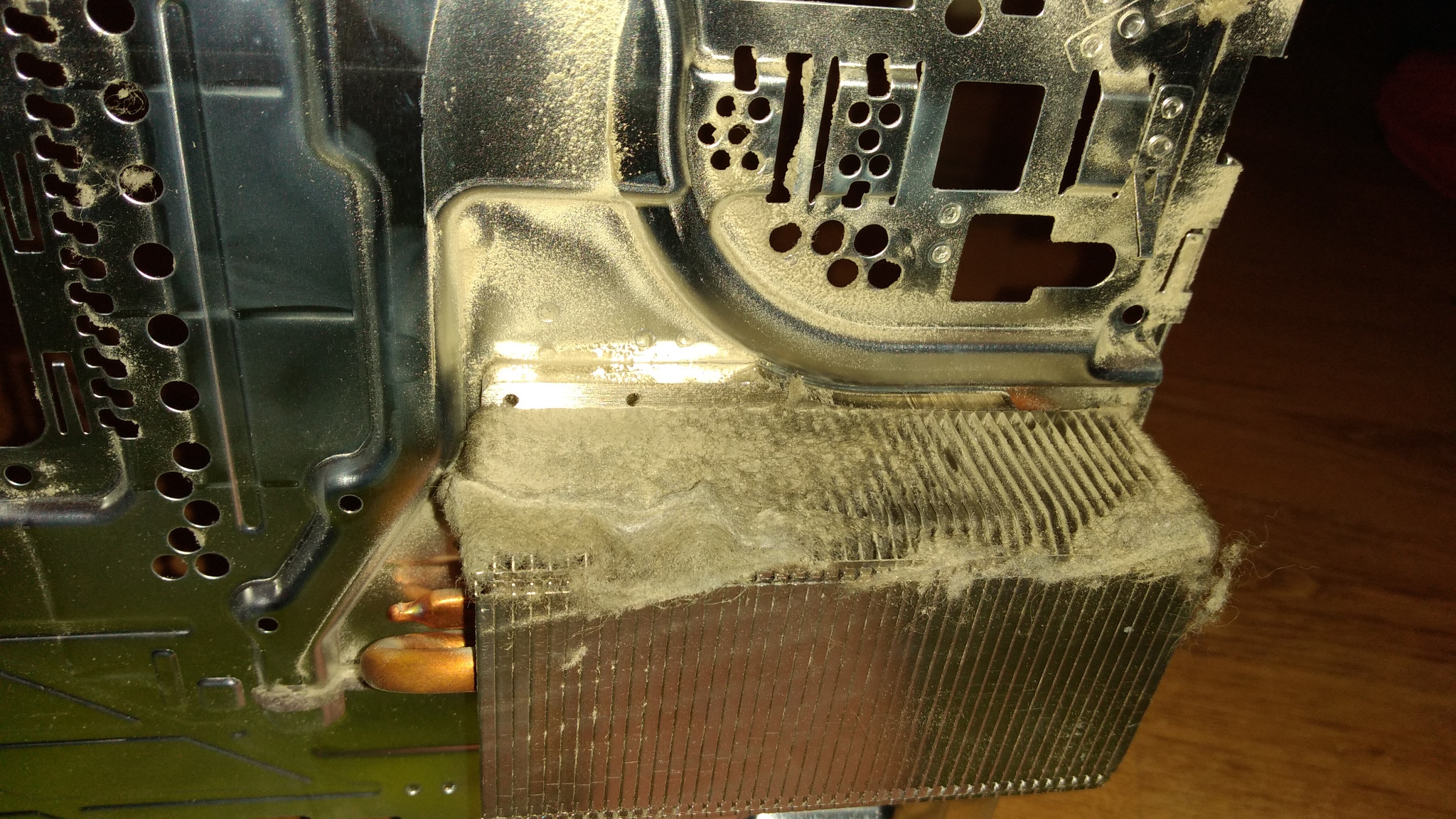 Zabrudzony kurzem radiator procesora z miedzianymi rurkami cieplnymi, widoczne metalowe elementy obudowy komputera.