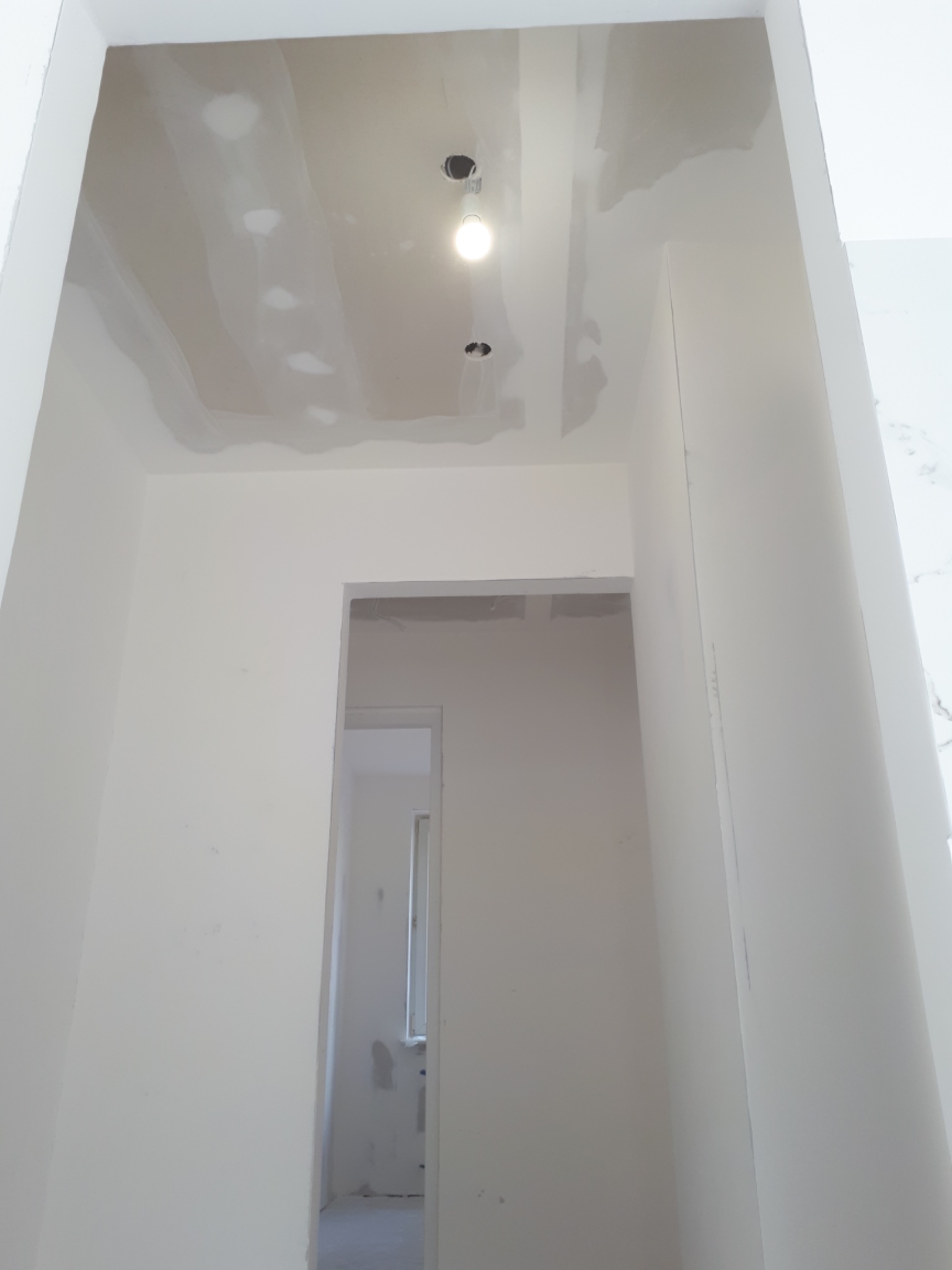 Wnętrze w trakcie prac wykończeniowych: sufit z widocznymi łączeniami płyt gipsowo-kartonowych przed położeniem gładzi, ściany przygotowane pod malowanie, widoczne otwory na oświetlenie.