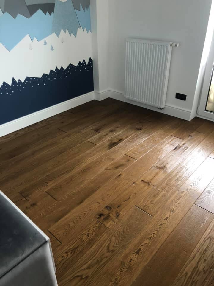 Ukończona podłoga z ciemnego drewna w pokoju dziecięcym z dekoracją ścienną w stylu górskim i grzejnikiem.