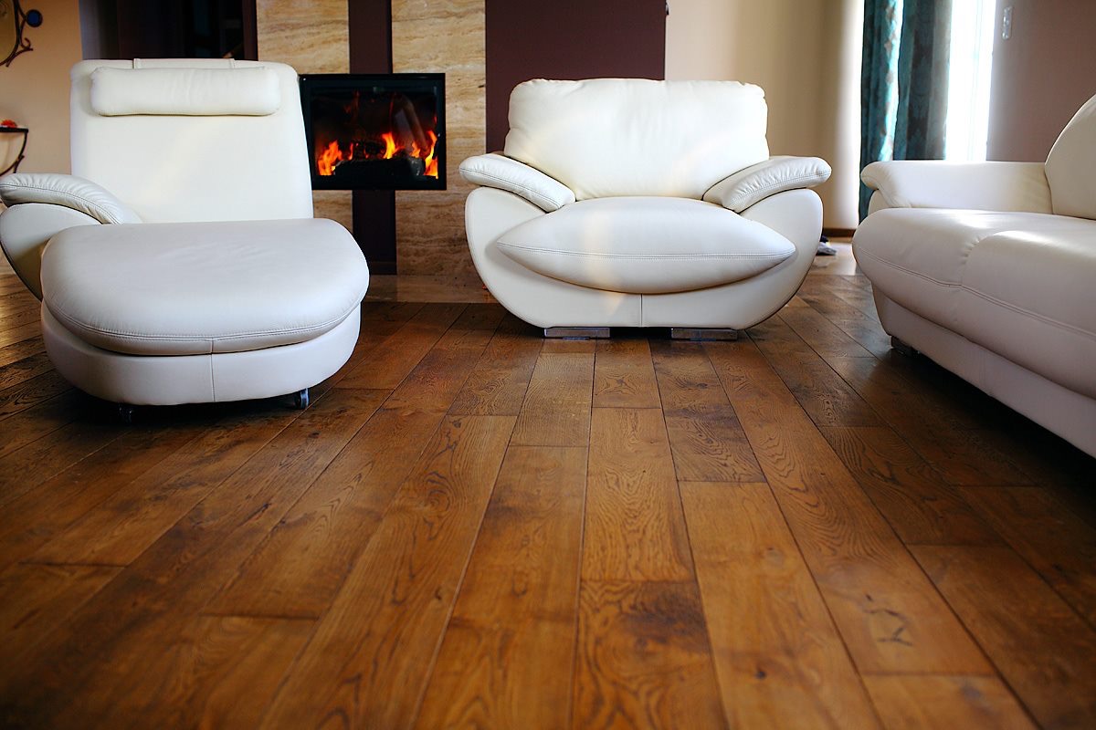 Ułożona podłoga z desek w salonie z białymi skórzanymi meblami i kominkiem z kamienia.
