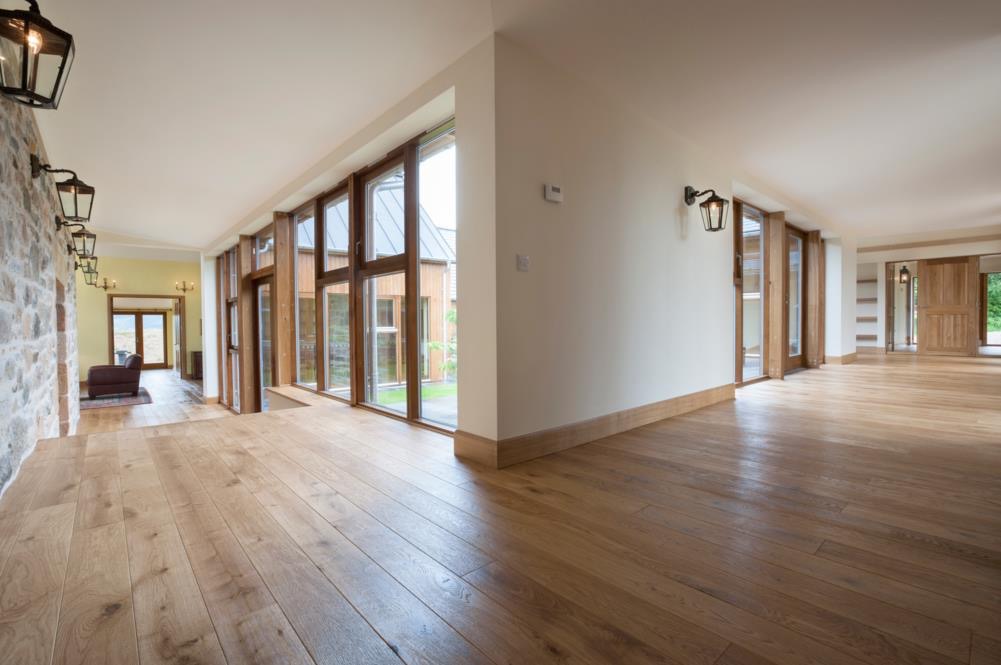 Jasna, dębowa podłoga ułożona w długim korytarzu z dużymi oknami i kamienną ścianą z ozdobnymi lampami.