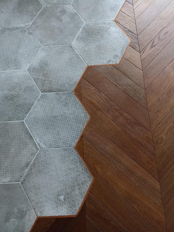 Połączenie podłogi z parkietu ułożonego w jodełkę i szarych heksagonalnych płytek z różnymi wzorami.