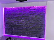 Ściana z dekoracyjnej cegły, podświetlona fioletowym światłem LED, tworząca nowoczesny efekt wizualny we wnętrzu.