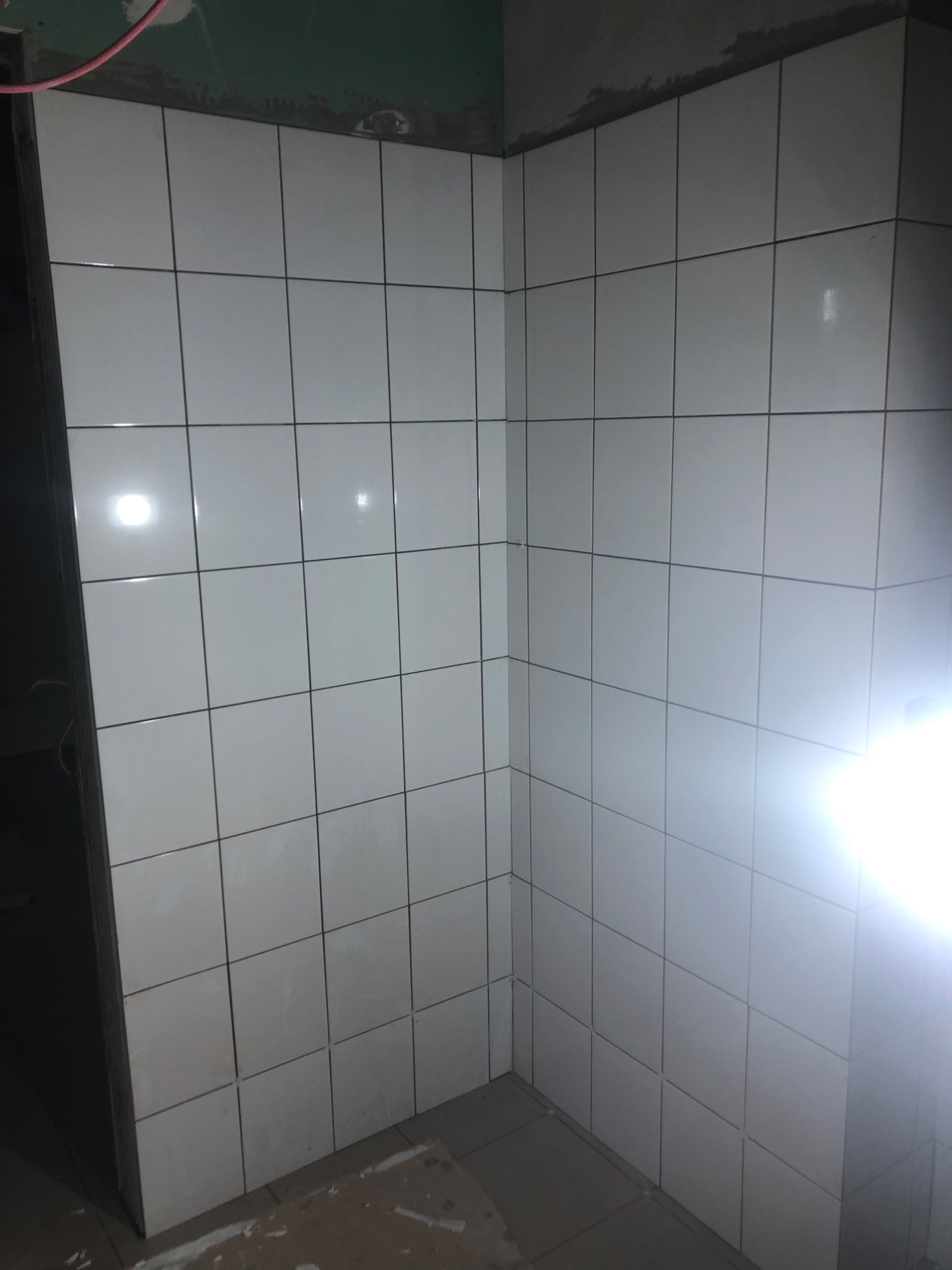 Świeżo położone białe, kwadratowe płytki w rogu pomieszczenia, widoczne szare fugi i niedokończone wykończenie przy suficie.