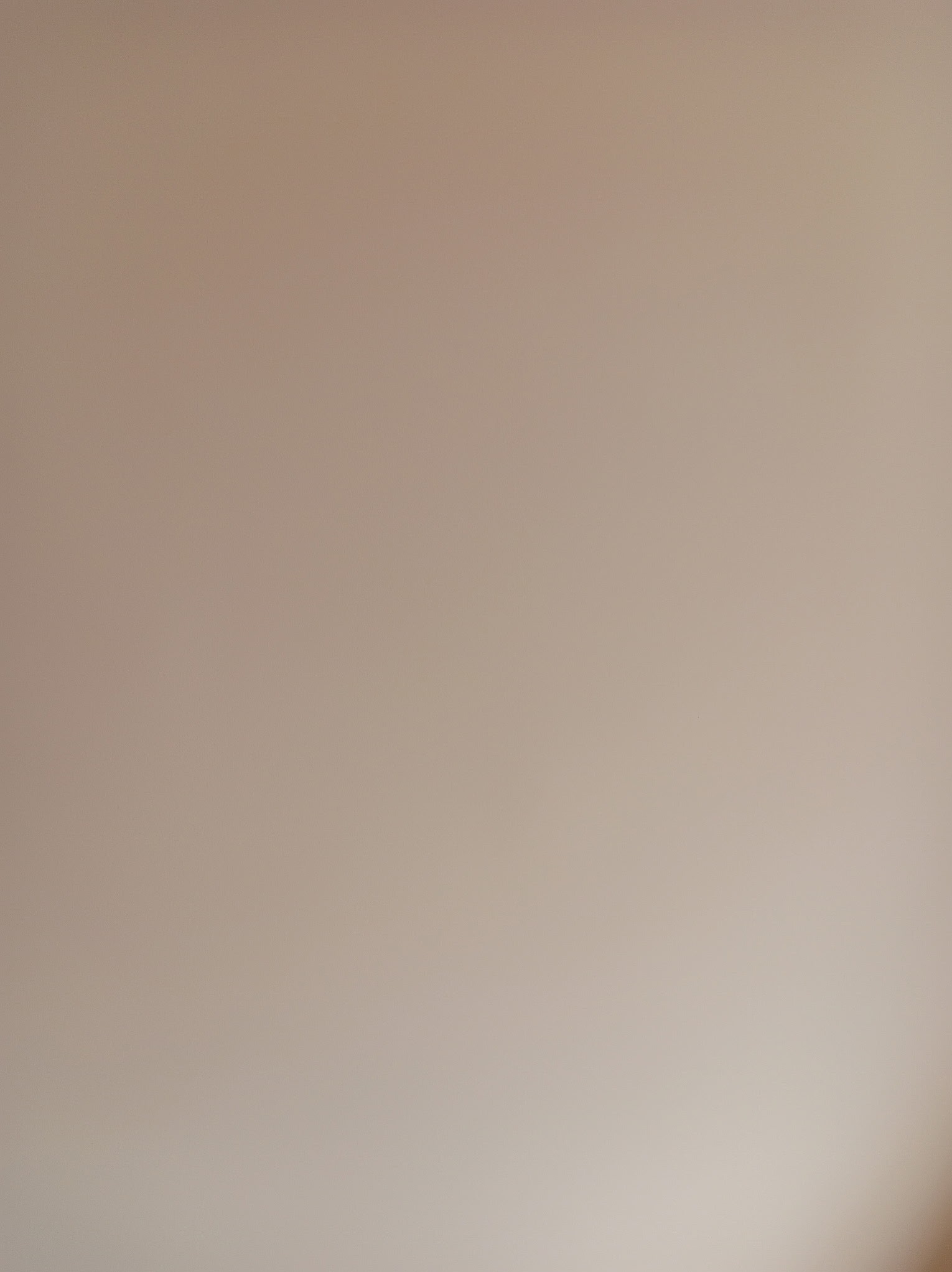 Beżowa, gładka ściana w delikatnym oświetleniu, ukazująca jednolitą strukturę i subtelne przejścia tonalne. Minimalistyczne ujęcie, idealne do prezentacji efektu malowania.