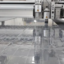 Precyzyjna maszyna tnąca ZUND wycina powtarzalny wzór w arkuszu transparentnego tworzywa sztucznego, widoczne liczne wgłębienia i refleksy świetlne na powierzchni materiału.