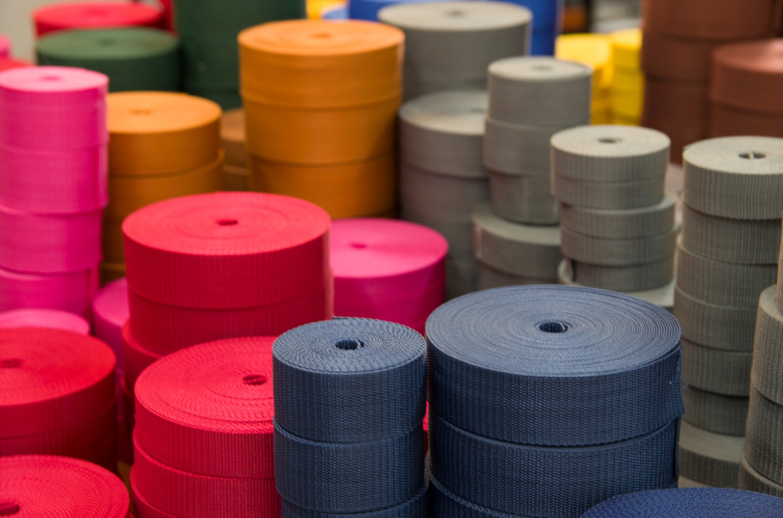Magazyn rolek taśmy parcianej w różnych kolorach: różowy, czerwony, niebieski, szary, pomarańczowy i zielony.