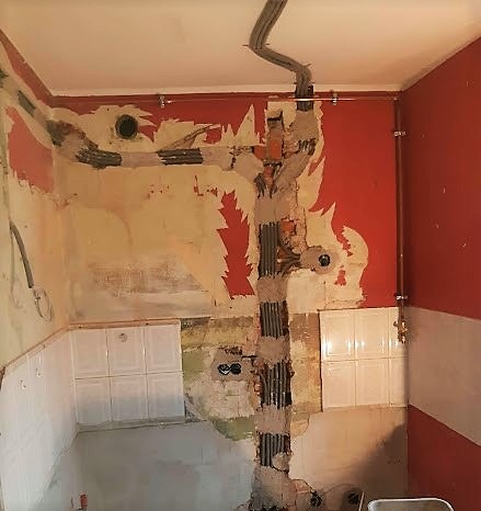 Wnętrze kuchni w trakcie remontu, widoczne kable elektryczne prowadzone w bruzdach ściennych, częściowo zamaskowane zaprawą, oraz fragment instalacji wodnej z rurami miedzianymi. Ściany w trakcie...