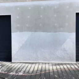 Fragment elewacji budynku z częściowo umytą powierzchnią, widoczne ślady po myciu oraz mokry drewniany taras z kablem ciśnieniowym.