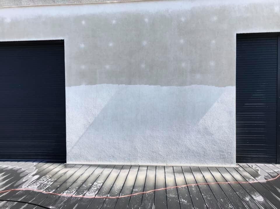 Fragment elewacji budynku z częściowo umytą powierzchnią, widoczne ślady po myciu oraz mokry drewniany taras z kablem ciśnieniowym.