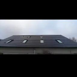 Ciemna dachówka ceramiczna na nowym dachu z oknami połaciowymi, widok z dołu na tle pochmurnego nieba.