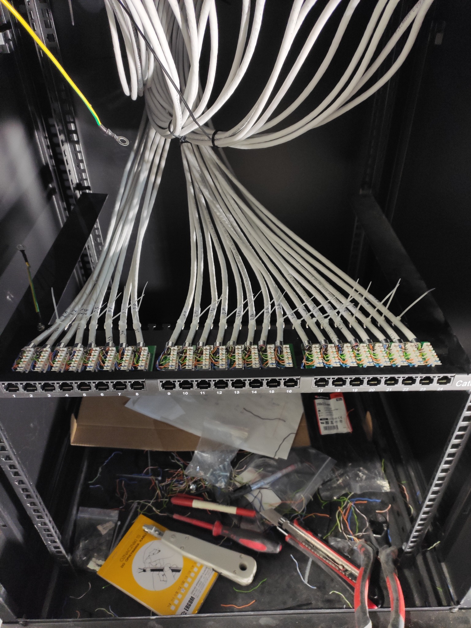 Panel krosowniczy z podłączonymi i oznaczonymi kablami w szafie rack, widoczne narzędzia i akcesoria na dolnej półce.