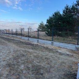 JAN-MET - Montaż siatki ogrodzeniowej na betonowej podmurówce, widoczny fragment terenu przed posesją z workiem i wystającą rurą wentylacyjną.