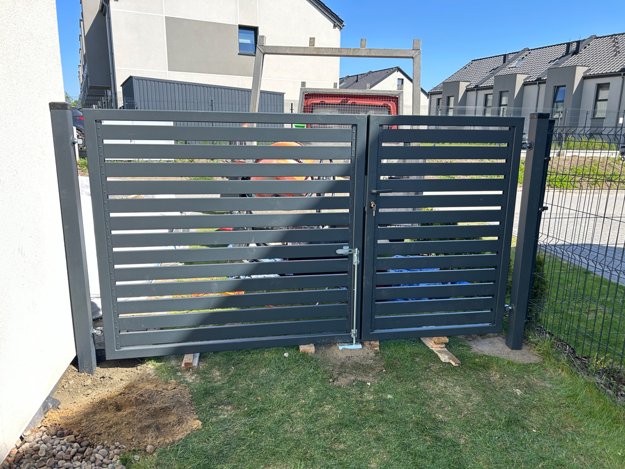 Nowoczesna, pozioma brama wjazdowa w kolorze grafitowym, z widoczną konstrukcją betonową w tle i mieszarką do betonu, sugerująca trwające prace montażowe.