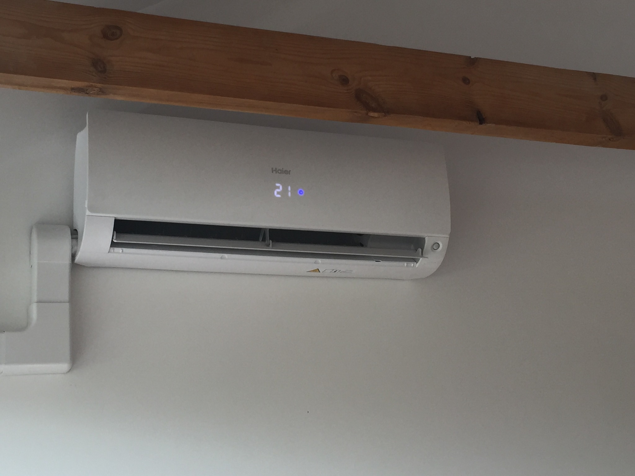 Zamontowany klimatyzator Haier z wyświetlaczem temperatury 21 stopni Celsjusza, widoczny na białej ścianie w pomieszczeniu z drewnianą belką stropową, Bielsk Podlaski.