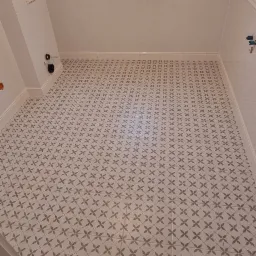 Wykończona łazienka z białymi płytkami ściennymi i podłogą w geometryczny wzór kwiatowy, widok z góry na okno dachowe.