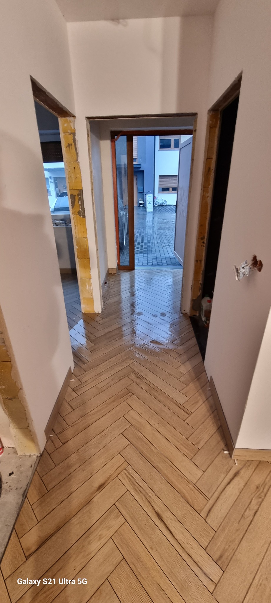 Korytarz w trakcie prac wykończeniowych z nową podłogą ułożoną w jodełkę, widoczne niedokończone ościeżnice i instalacja elektryczna.