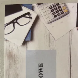 Biurko z kalkulatorem, okularami i dokumentami na tle imitującym drewno.