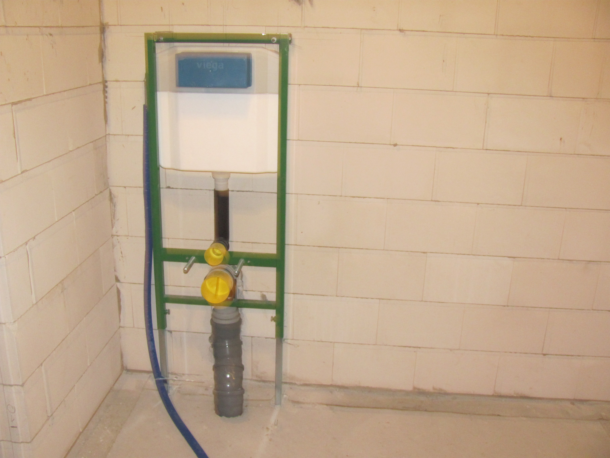 Stelaż podtynkowy WC Viega z widocznymi elementami instalacji hydraulicznymi, w surowym stanie przed zabudową, na tle ściany z białych bloczków.