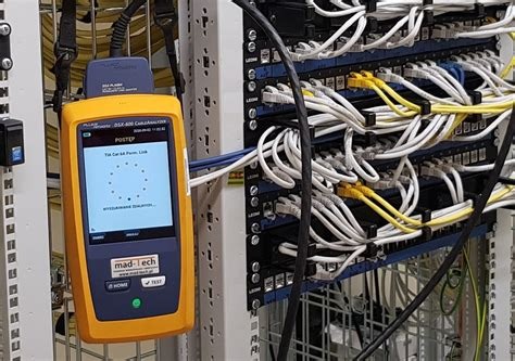 Miernik Fluke DSX-602 CableAnalyzer podczas testowania okablowania strukturalnego w szafie rack, widoczne patch panele i kable zakończone wtykami RJ45.
