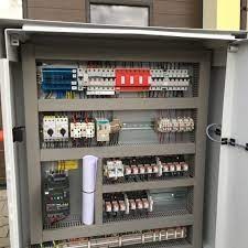 Otwarta szafa sterownicza z widocznymi bezpiecznikami, przekaźnikami i okablowaniem. Elementy ułożone w regularny sposób na szarych szynach montażowych. Zastosowano różne kolory przewodów...