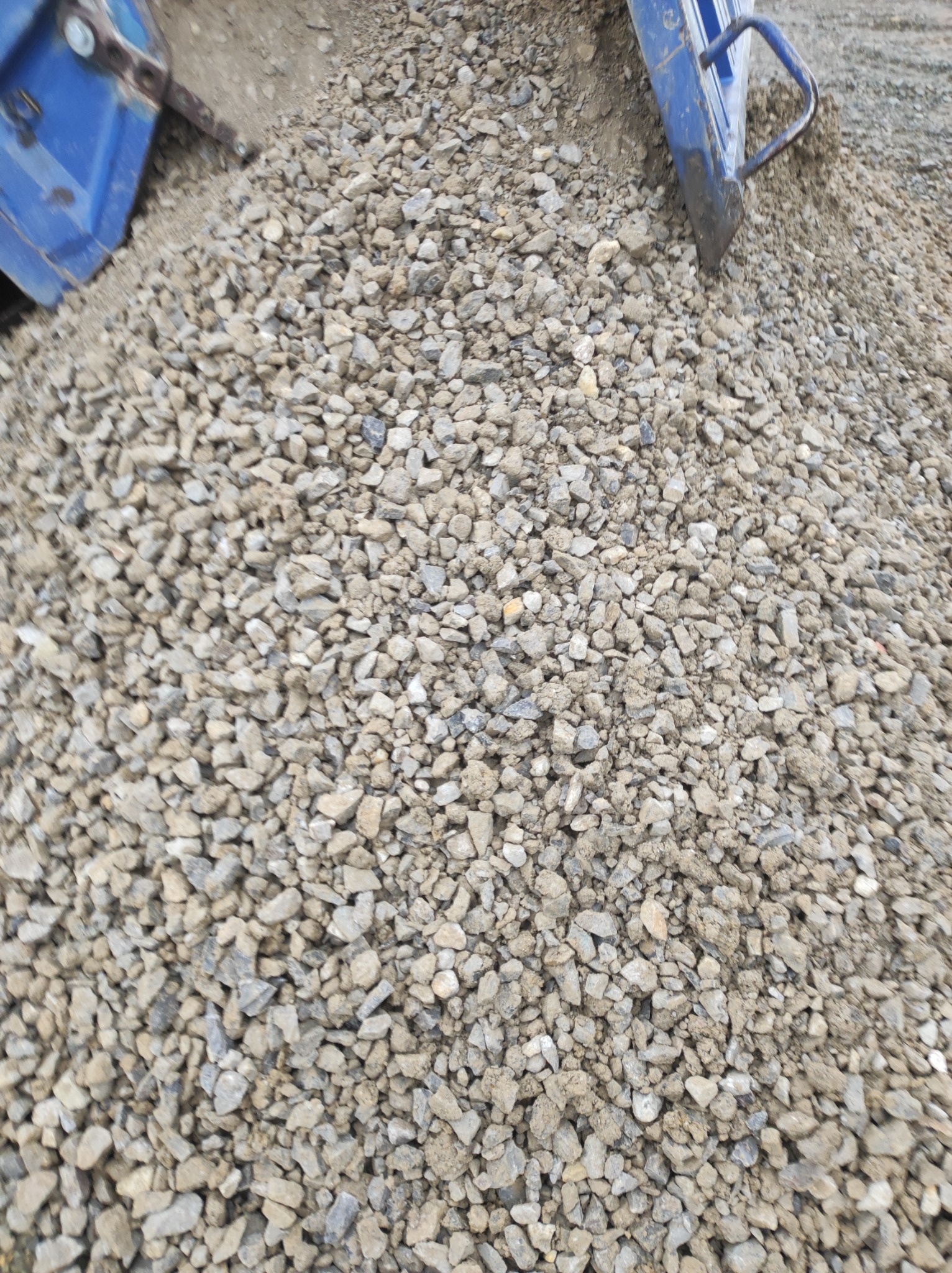 Kupa drobnego, szarego kruszywa z fragmentami niebieskiej maszyny budowlanej w górnej części kadru.