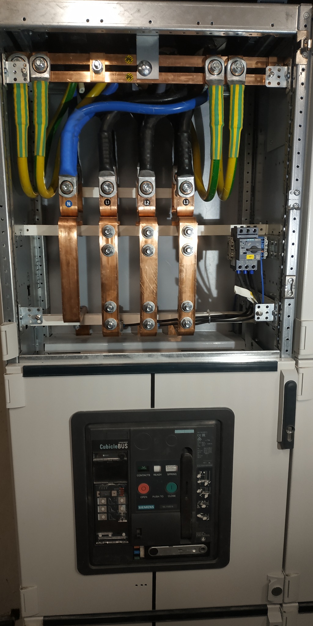 Wewnętrzny widok rozdzielnicy elektrycznej z miedzianymi szynami zbiorczymi oznaczonymi N, L1, L2, L3, przewodami w izolacji żółto-zielonej i niebieskiej, oraz wyłącznikiem Siemens CubicleBUS...
