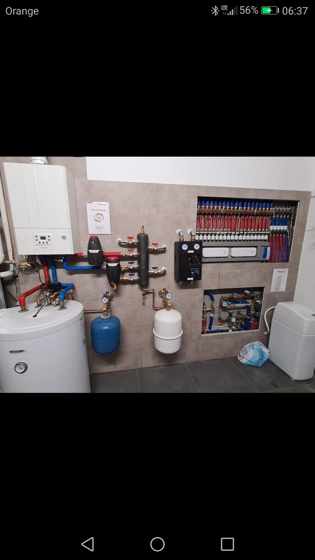 Kompletna kotłownia z piecem gazowym, zbiornikiem CWU, rozdzielaczem ogrzewania podłogowego w zabudowie oraz naczyniami przeponowymi, na tle płytek imitujących kamień.