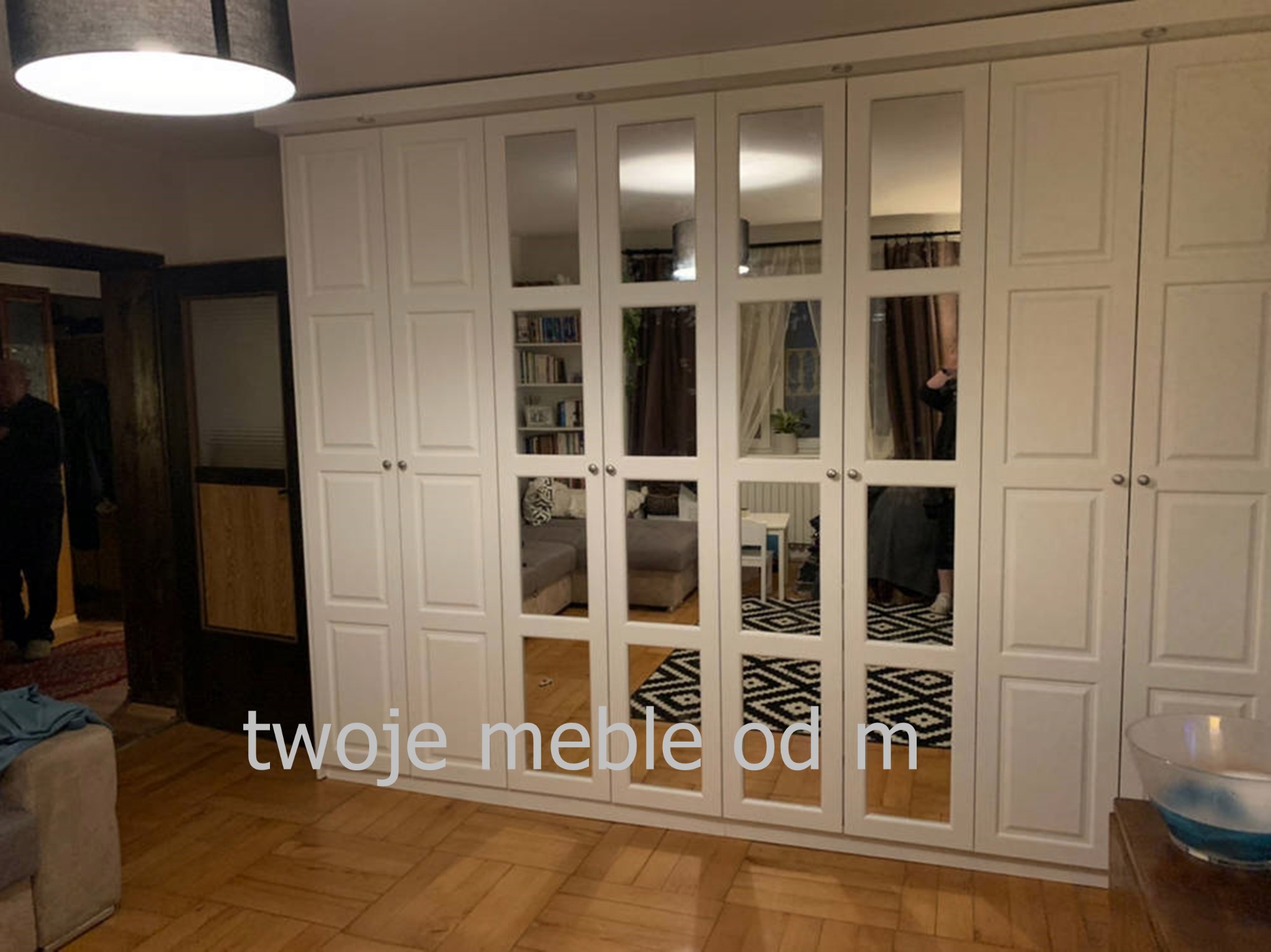 Biała szafa z lustrami w Radomsku, odbijająca fragment salonu z sofą i wzorzystym dywanem.