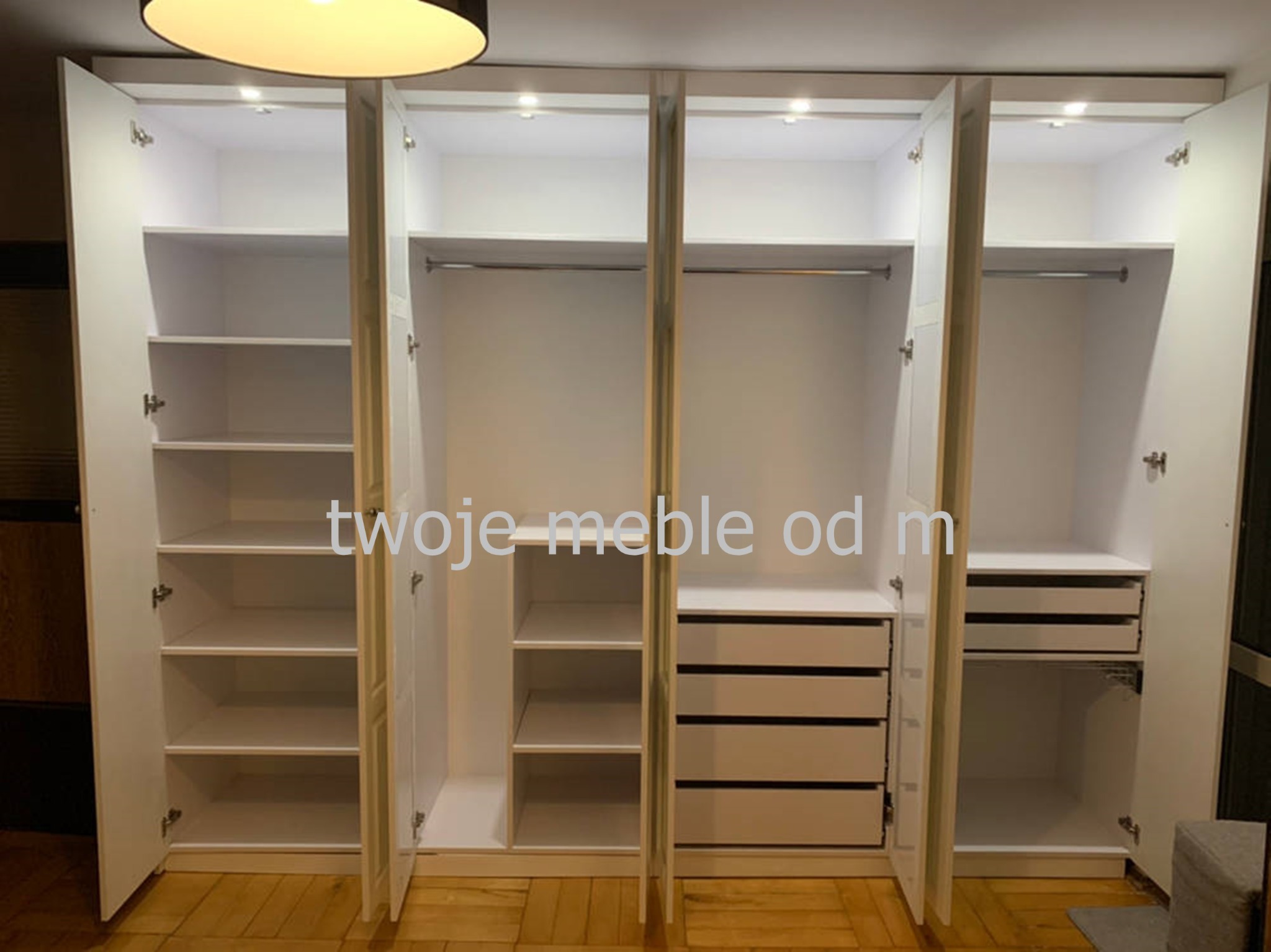 Biała szafa wnękowa z otwartymi drzwiami, ukazująca półki, drążki na ubrania i szuflady, oświetlona od wewnątrz punktowymi lampkami LED.