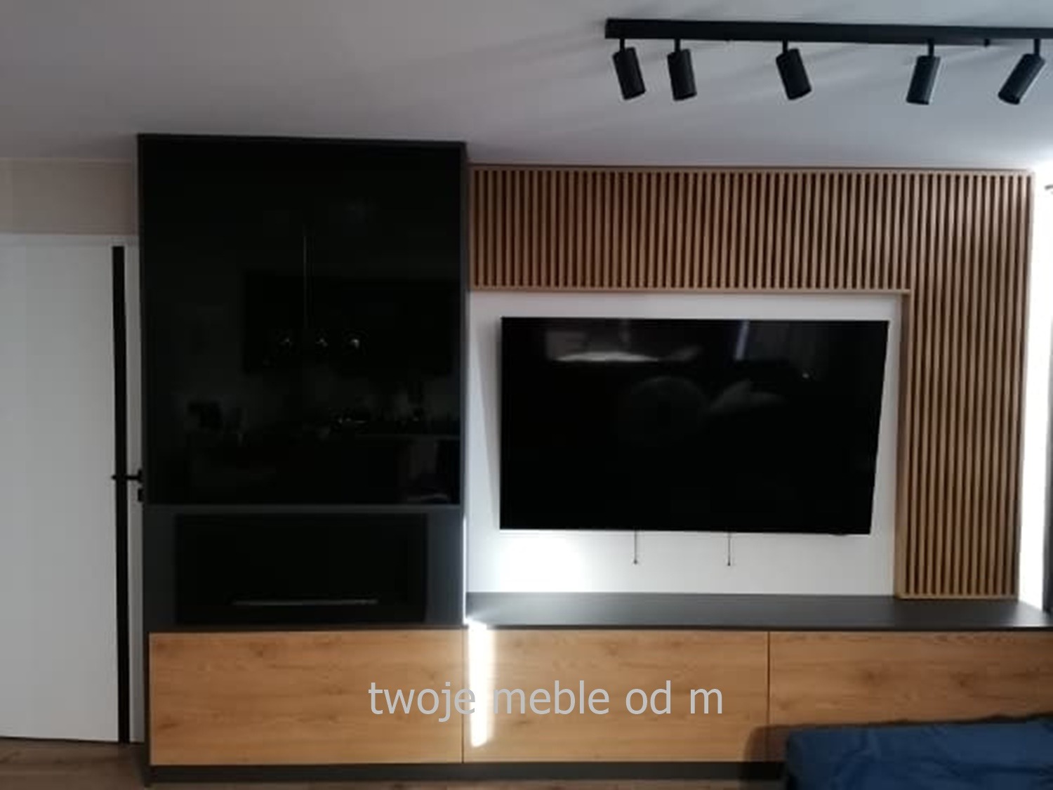 Nowoczesna zabudowa ściany telewizyjnej z lakierowanym na czarno modułem, drewnianymi lamelami i szafkami z forniru dębowego podświetlonymi punktowo