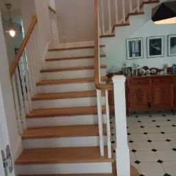 Drewniane schody z białymi balustradami w domu w Lublinie, widok z dołu na pierwsze stopnie, parkiet w czarno-białą szachownicę.