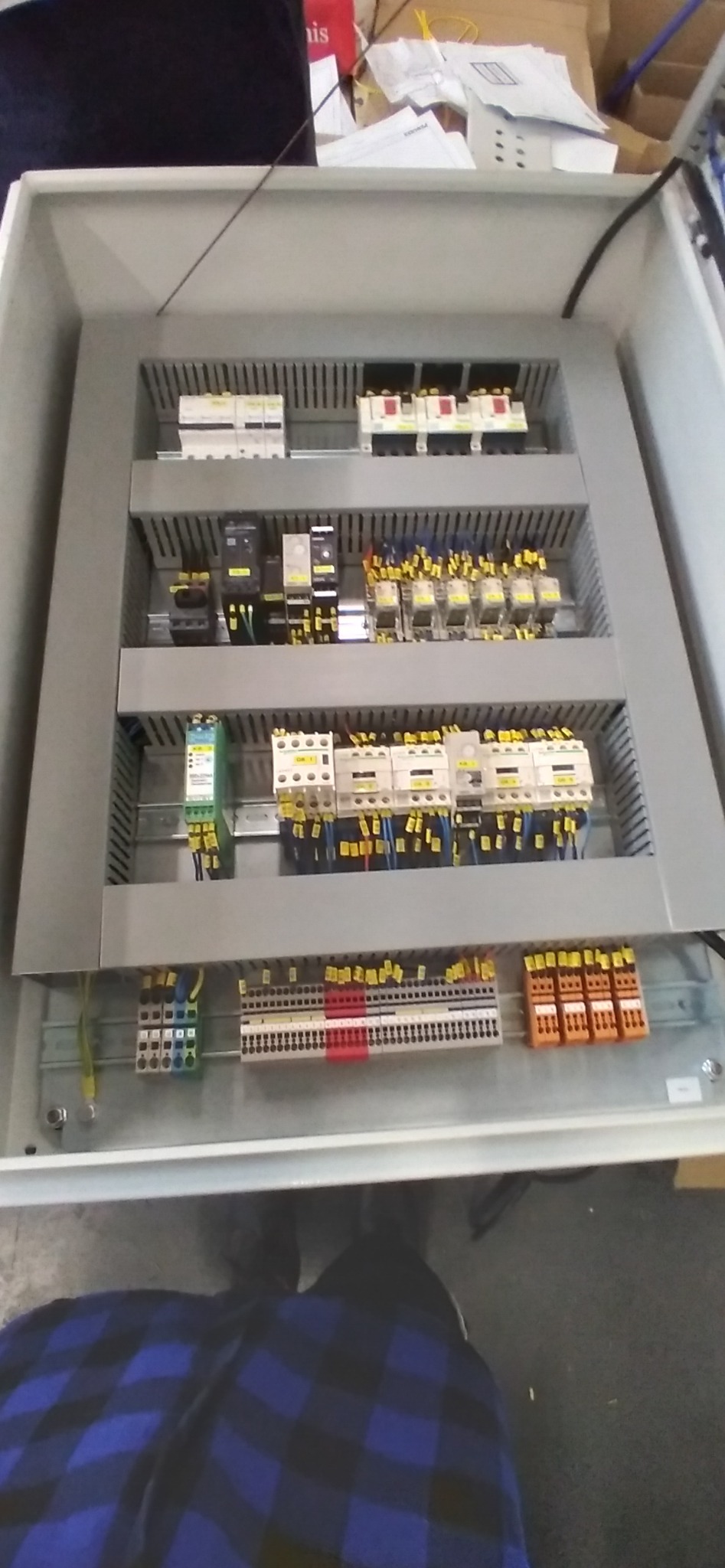 Wewnętrzny widok szarej szafy sterowniczej z zamontowanymi bezpiecznikami, przekaźnikami i listwami zaciskowymi, z widocznymi przewodami z oznaczeniami.