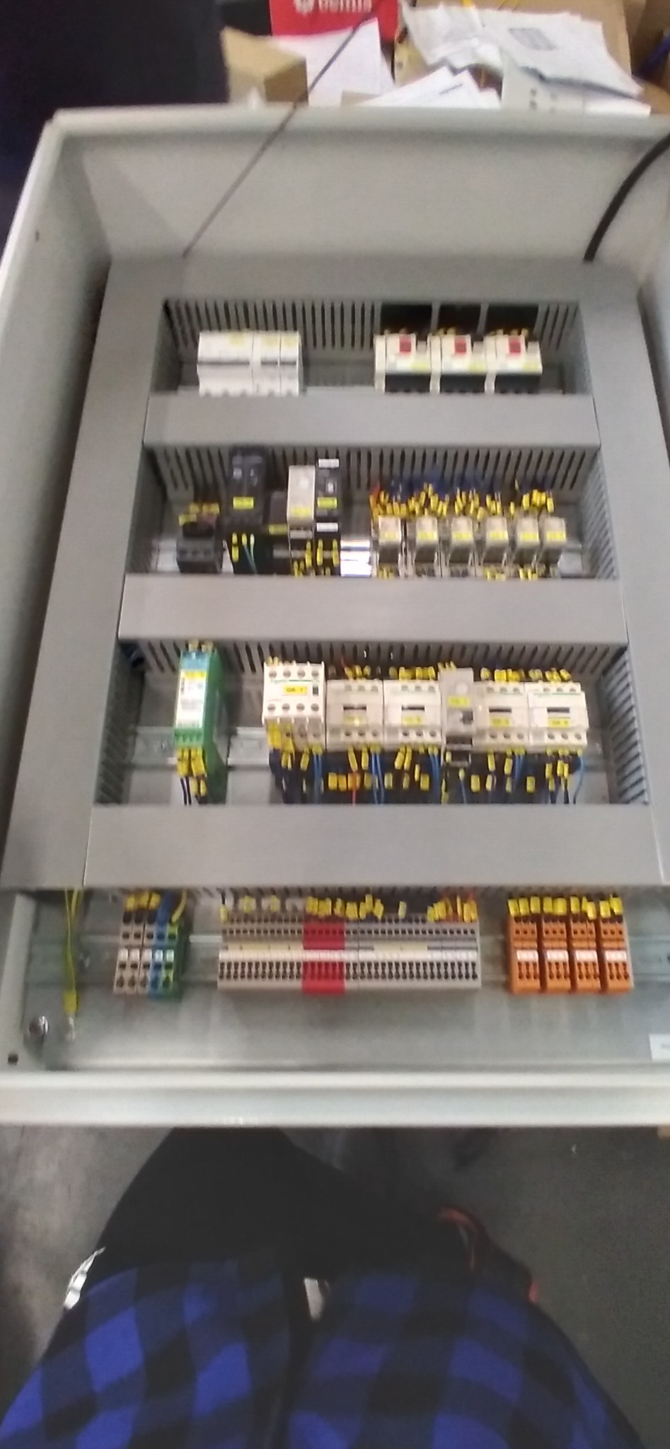 Wnętrze szarej szafy sterowniczej z zamontowanymi bezpiecznikami, stycznikami i listwami zaciskowymi z przewodami w kolorach żółtym, niebieskim i zielonym.