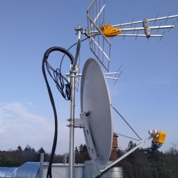 ELMYK SPÓŁKA Z OGRANICZONĄ ODPOWIEDZIALNOŚCIĄ - Anteny telewizyjne i satelitarne zamontowane na dachu budynku z widocznymi przewodami i elementami instalacji wentylacyjnej w tle.