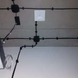 Czarna instalacja kablowa przymocowana do sufitu, z widoczną puszką rozgałęźną, punktem dostępowym Wi-Fi i fragmentem wentylacji.