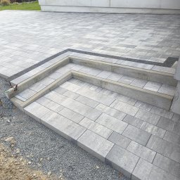 MW Bau Marcel Wende - Ułożona z szarych kostek brukowych ścieżka z dwoma stopniami, obrzeże z ciemnego grysu, widoczne niedokończone prace i rozsypany żwir.