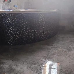 Zaokrąglona obudowa wanny wykończona mozaiką w odcieniach szarości i czerni, dopasowana do szarej, błyszczącej podłogi z płytek w łazience, widoczne baterie i fragment wanny.