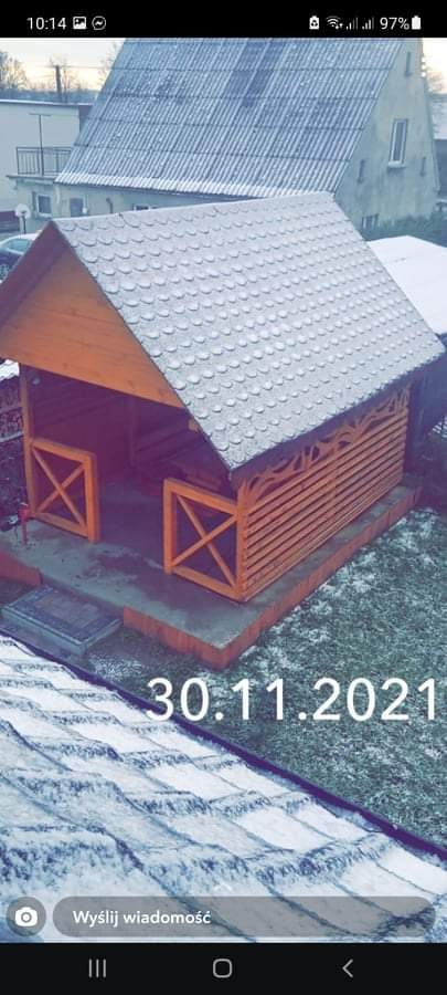 Drewniana altana ogrodowa z dachem pokrytym gontem bitumicznym, widoczna z góry na tle zaśnieżonego ogrodu i budynku mieszkalnego.