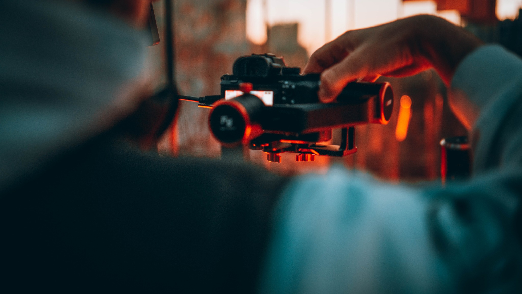 Operator filmowy obsługuje kamerę z czerwonym obiektywem i monitorem, ustawioną na statywie, w tle rozmyte światła.